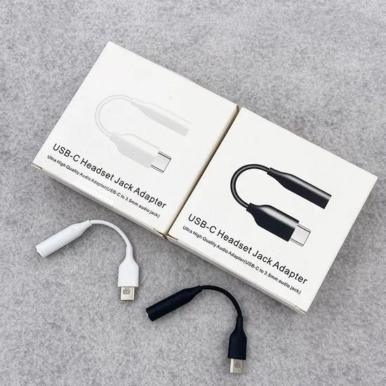 White and black USB-C to 3.5mm headphone jack adapters laid beside their two retail boxes.